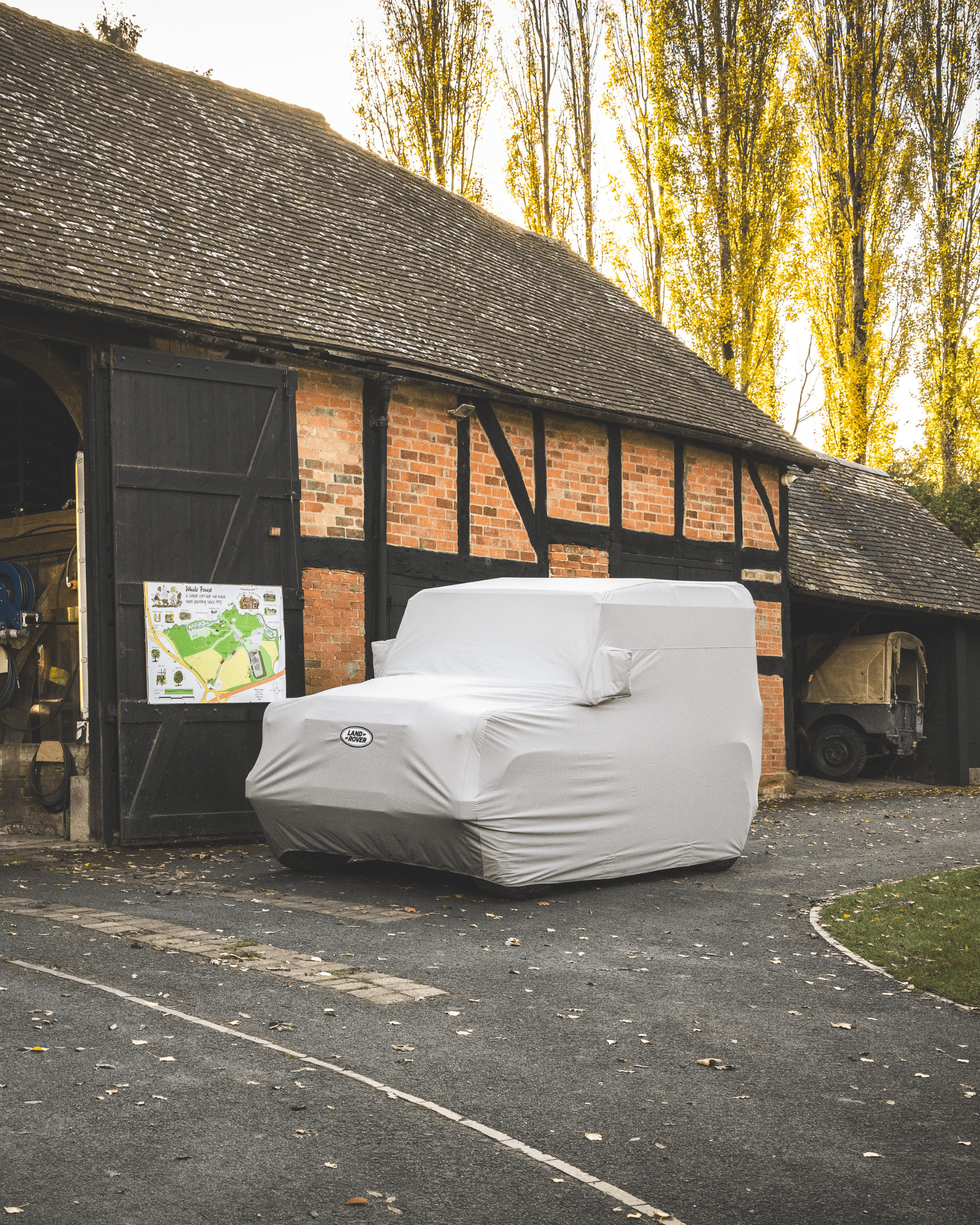 Covered Land Rover outside rustic brick-and-timber garage with map sign on door.
