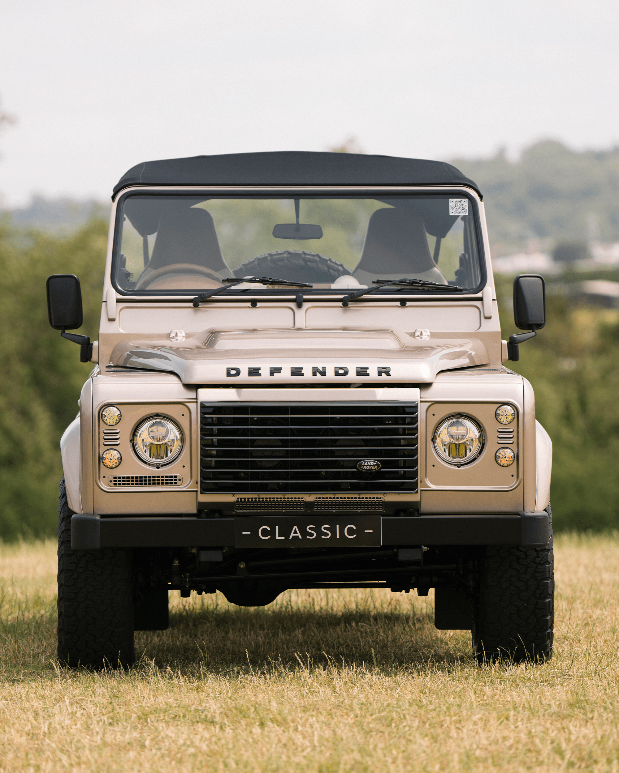 Front view of a beige Land Rover Defender with 'DEFENDER' and 'CLASSIC' plate, parked on grass.
