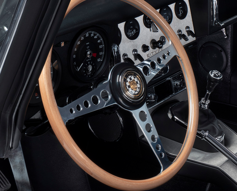 Classic E-Type interior with wooden steering wheel and dashboard gauges.