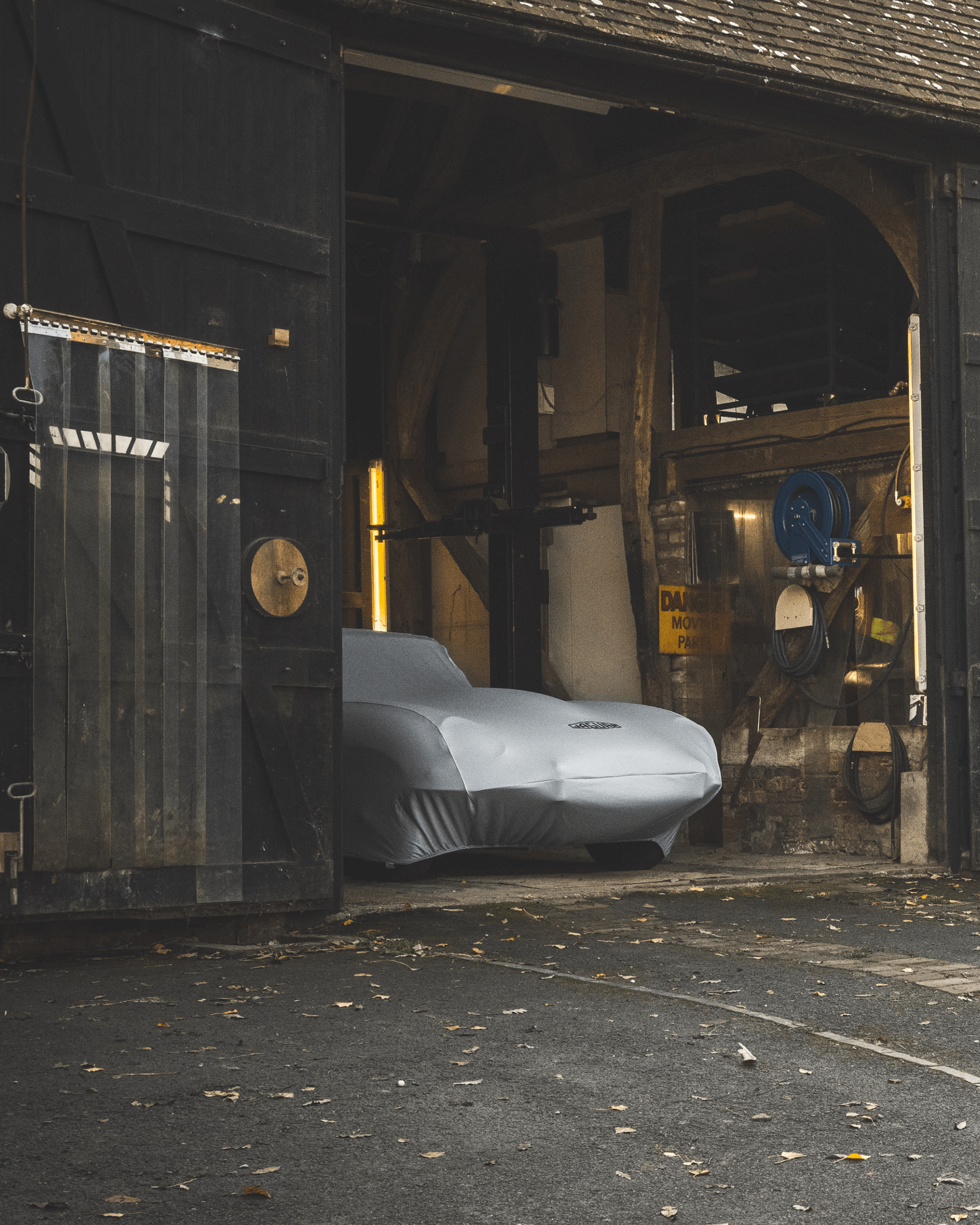 Partially open garage door revealing a Jaguar under grey car cover with tools mounted on walls.