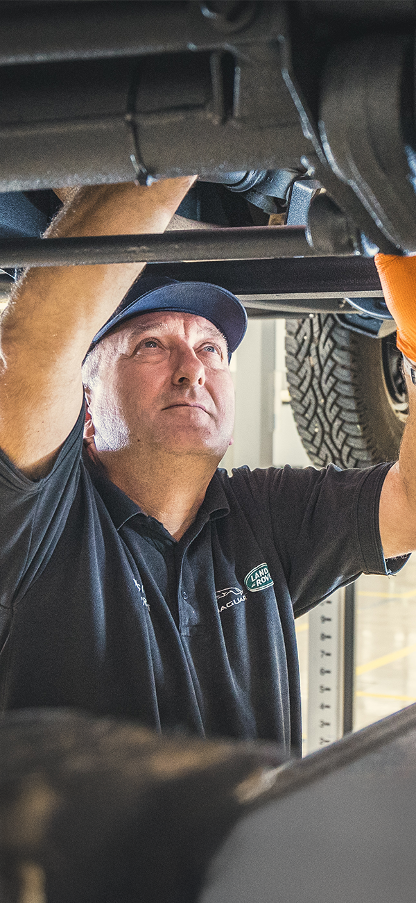 Person in orange gloves working under a vehicle in an automotive workshop.