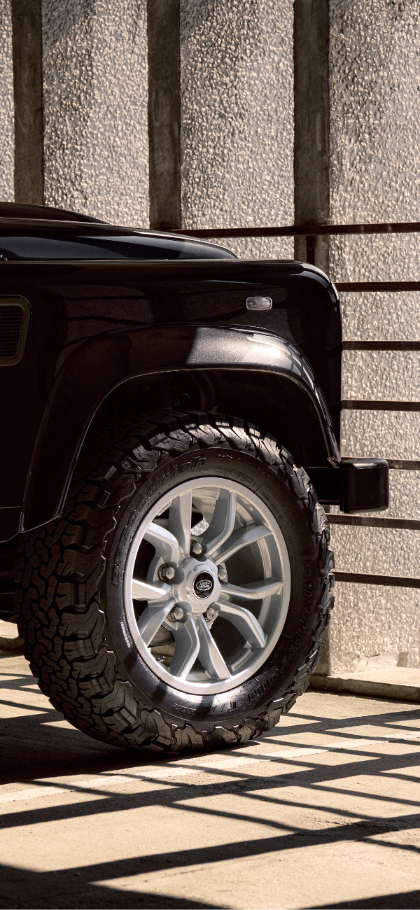 Front right tire of a black Defender in a shadowed concrete setting.