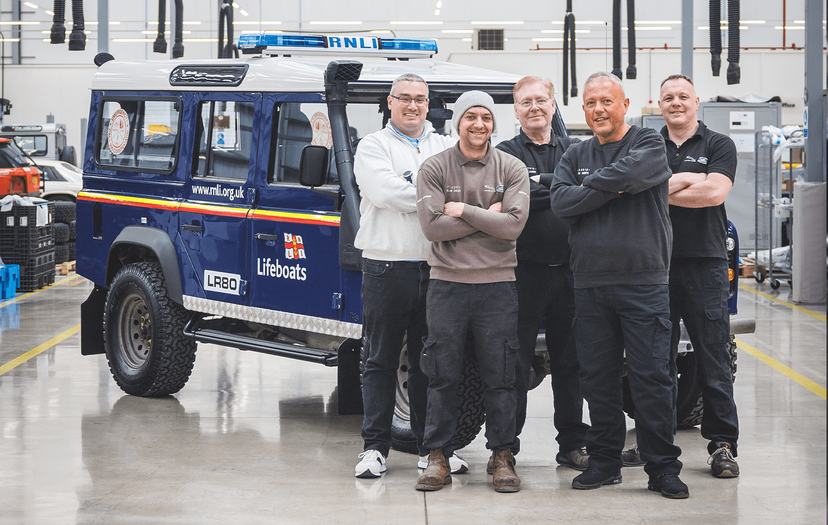 Five people standing in front of RNLI Lifeboats vehicle in workshop setting.