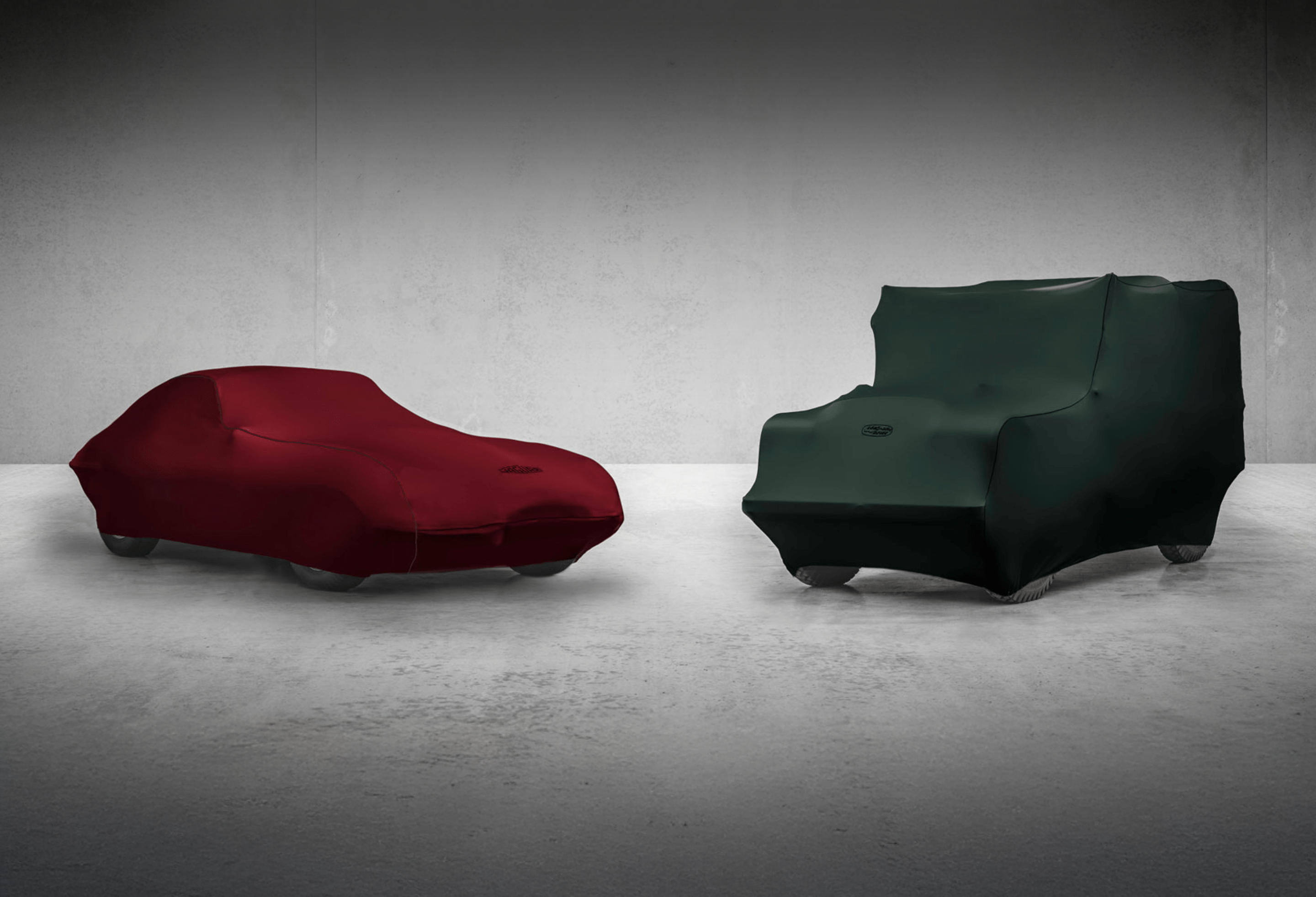 Classic Jaguar and Land Rover covered with fabric car cover in minimalist concrete room.