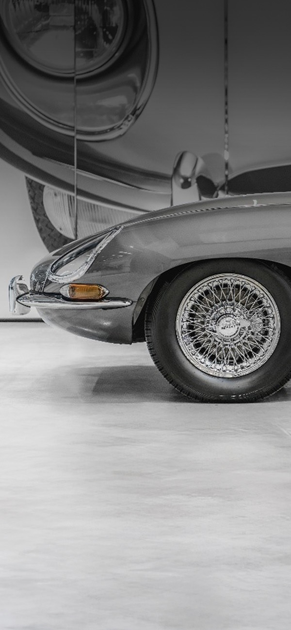 Front view of vintage green Land Rover and grey Jaguar E-Type facing each other in a showroom.