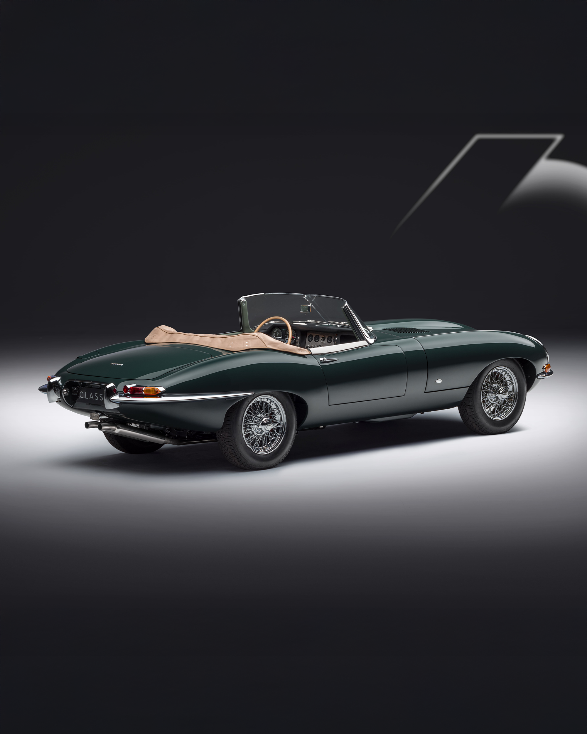 Dark green E-Type convertible with beige interior, rear-side view on dark background.