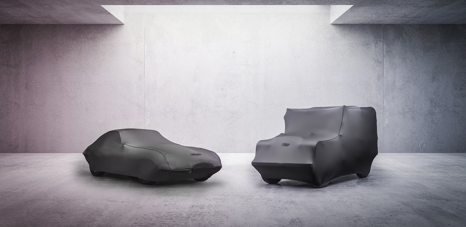 Classic Jaguar and Land Rover covered with fabric car cover in minimalist concrete room.